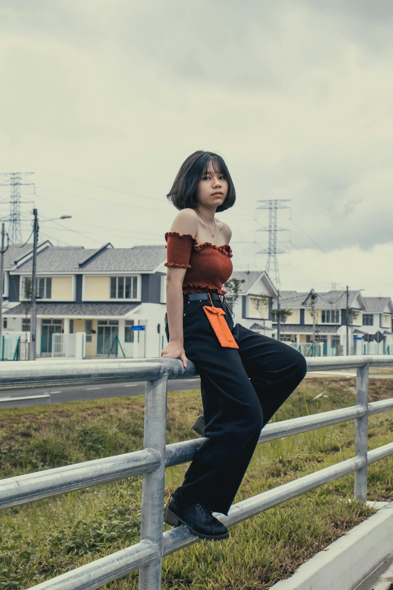 Young woman posing stylishly against a suburban backdrop, wearing trendy attire.