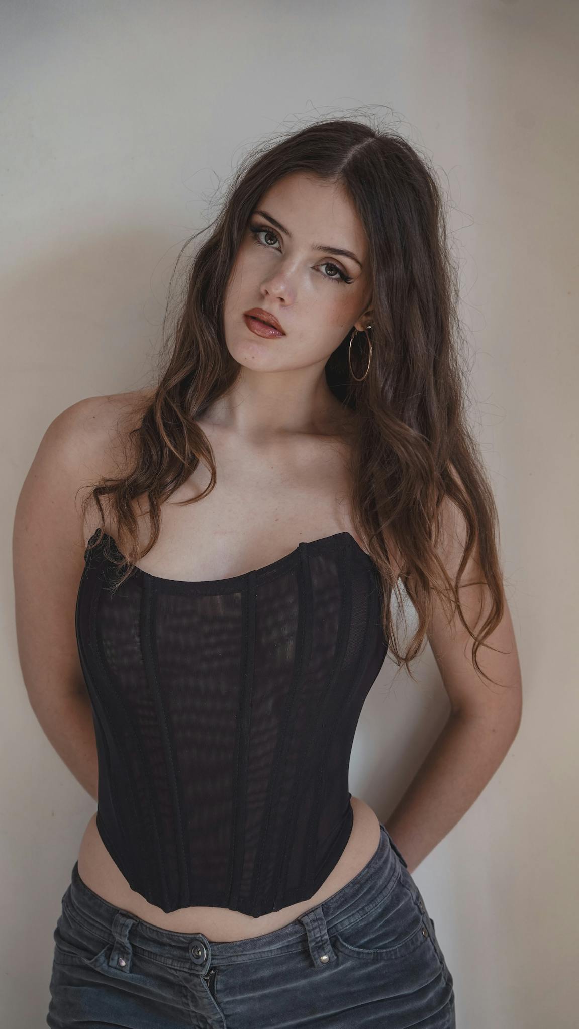 Portrait of a young woman with long hair wearing a black corset and jeans, looking confident.