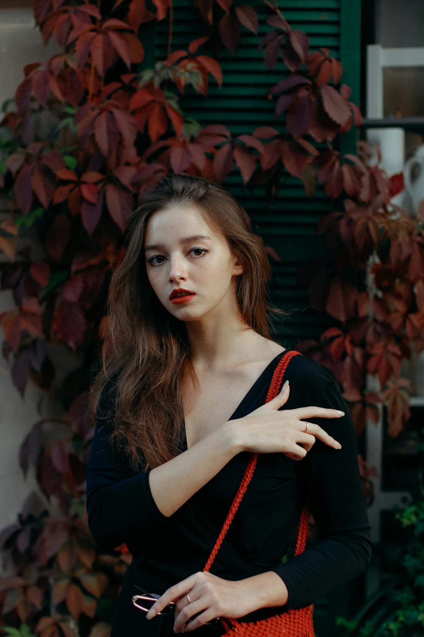 Stylish woman posing outdoors with autumnal foliage background, exuding elegance and modern fashion sense.